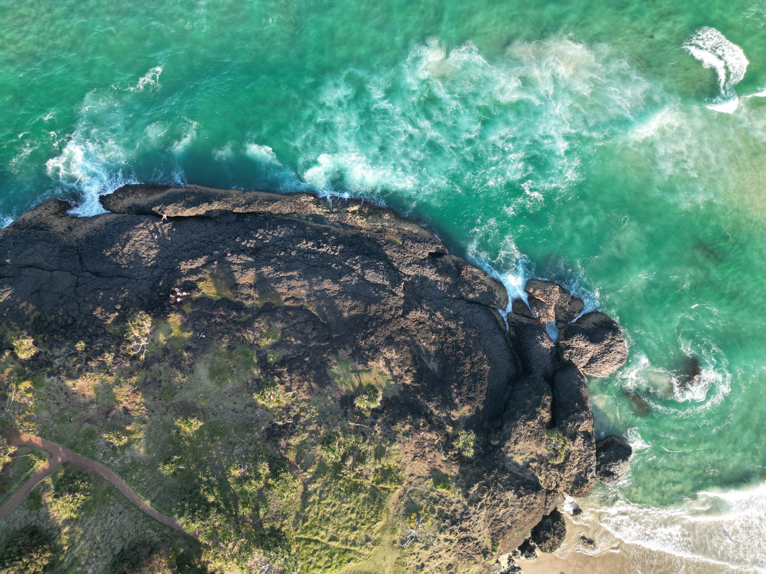 Aerial view of a rocky coastline with turquoise sea and a winding road along the shore of the landmass.