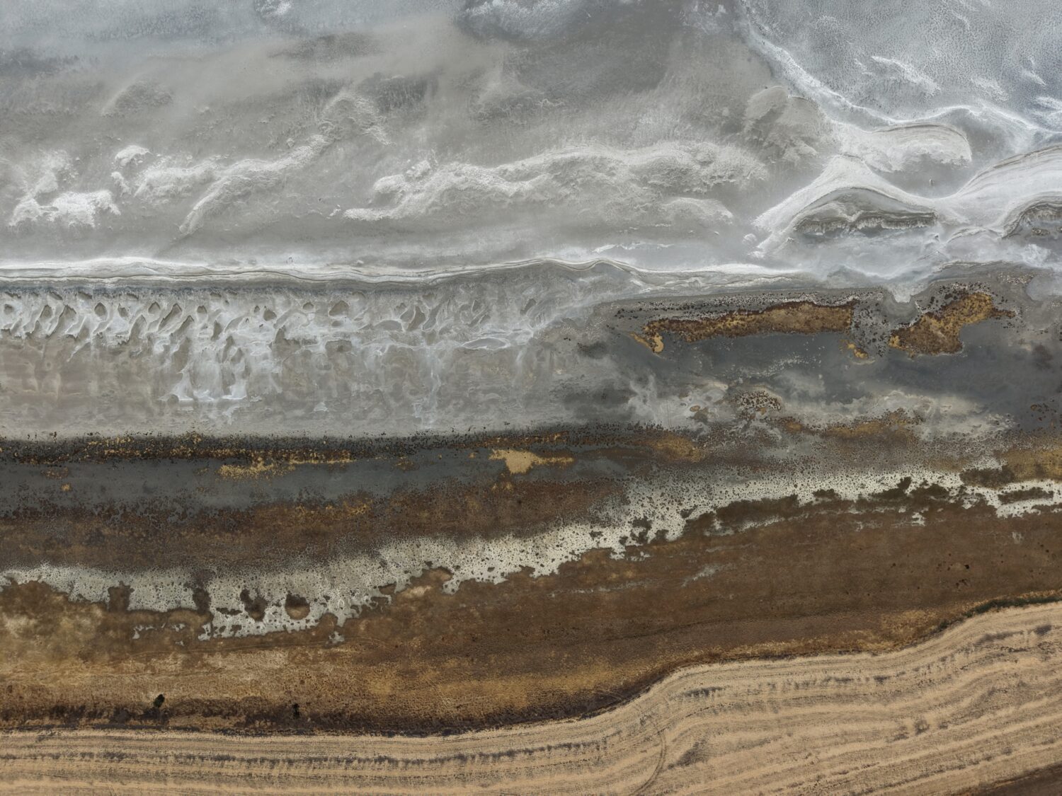 Aerial view of layered sedimentary strata in gray, white, and brown tones with wavy patterns.